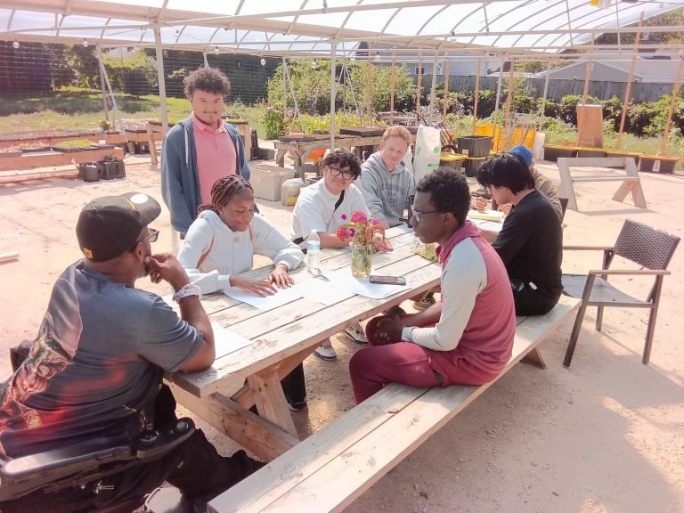 New Village Academy interns working with Randy and Dan at a picnic table in the greenhouse